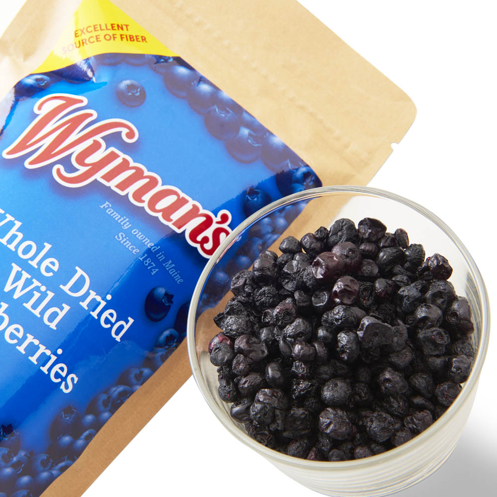 Woman's Whitney whole dried Wild Blueberry snack in a glass next to a bag.