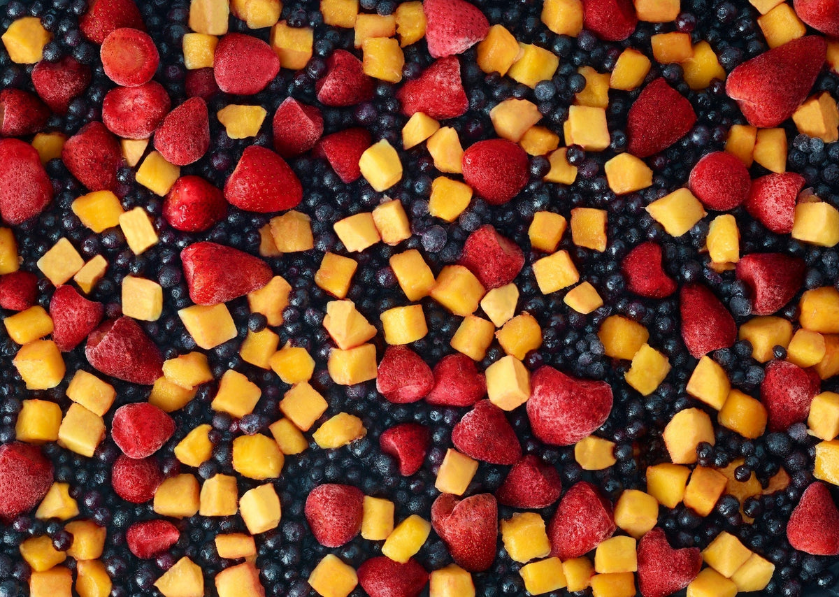 An overhead view of a colorful mix of frozen strawberries, blueberries, and mango chunks spread out in an even layer.