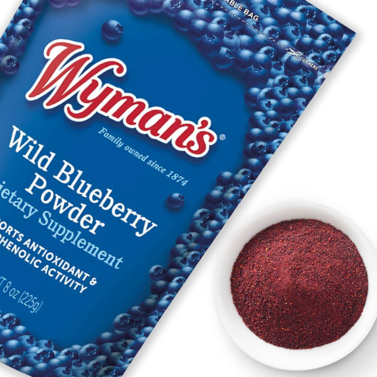 Wyman's Wild Blueberry Powder package in blue with the Wyman's logo, shown alongside a white bowl filled with dried blueberries on a white background.