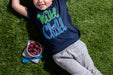 A boy lying on the grass with a bowl of Wyman's Wild Child Kids T-shirt blueberries.